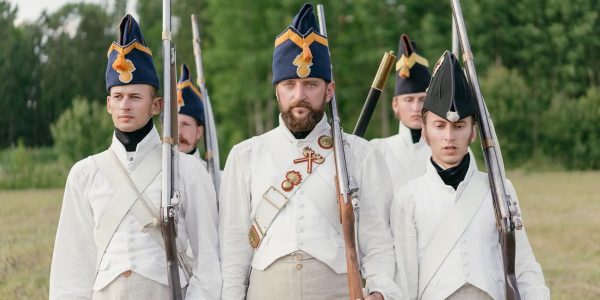 Soldiers marching in historical military uniforms reenact past events outdoors.